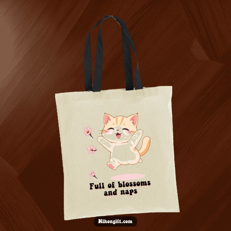 Funny tote bag featuring a fluffy cat joyfully leaping with abandon to catch a delicate cherry blossom petal floating in the air.